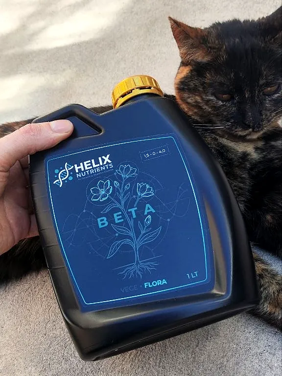 Envase HELIX BETA de 1 L sostenido a mano, con una gata carey apoyada detrás, foto real